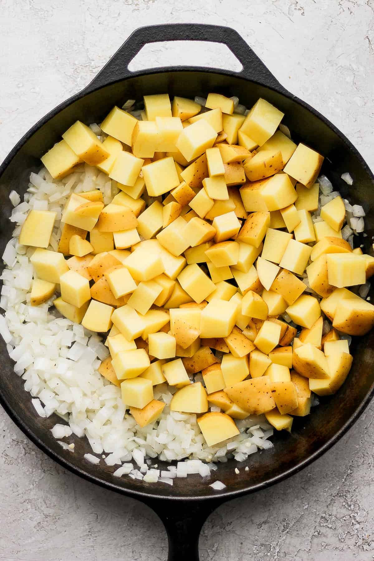 Cubed potatoes in the cast iron skillet along with onion, garlic, and butter.