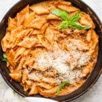 Cast iron skillet filled with creamy tomato pasta topped with freshly grated parmesan cheese and 4 fresh basil leaves.