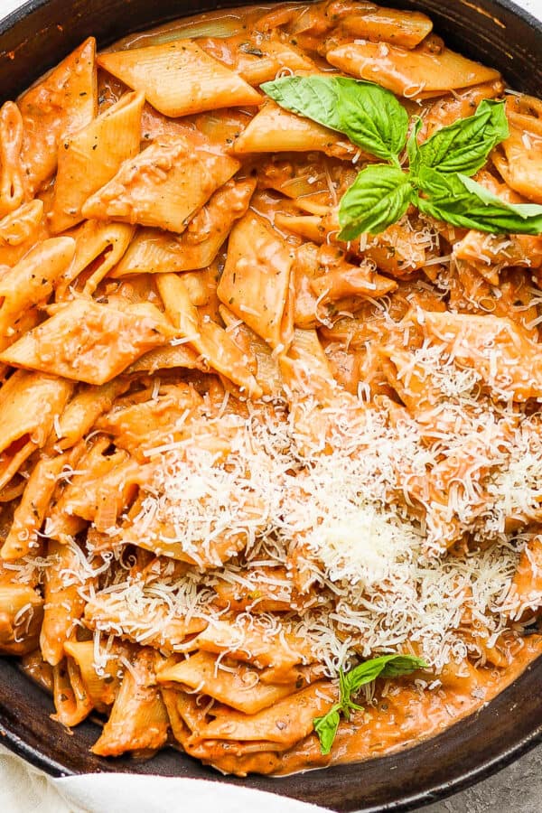 Cast iron skillet filled with creamy tomato pasta topped with freshly grated parmesan cheese and 4 fresh basil leaves.