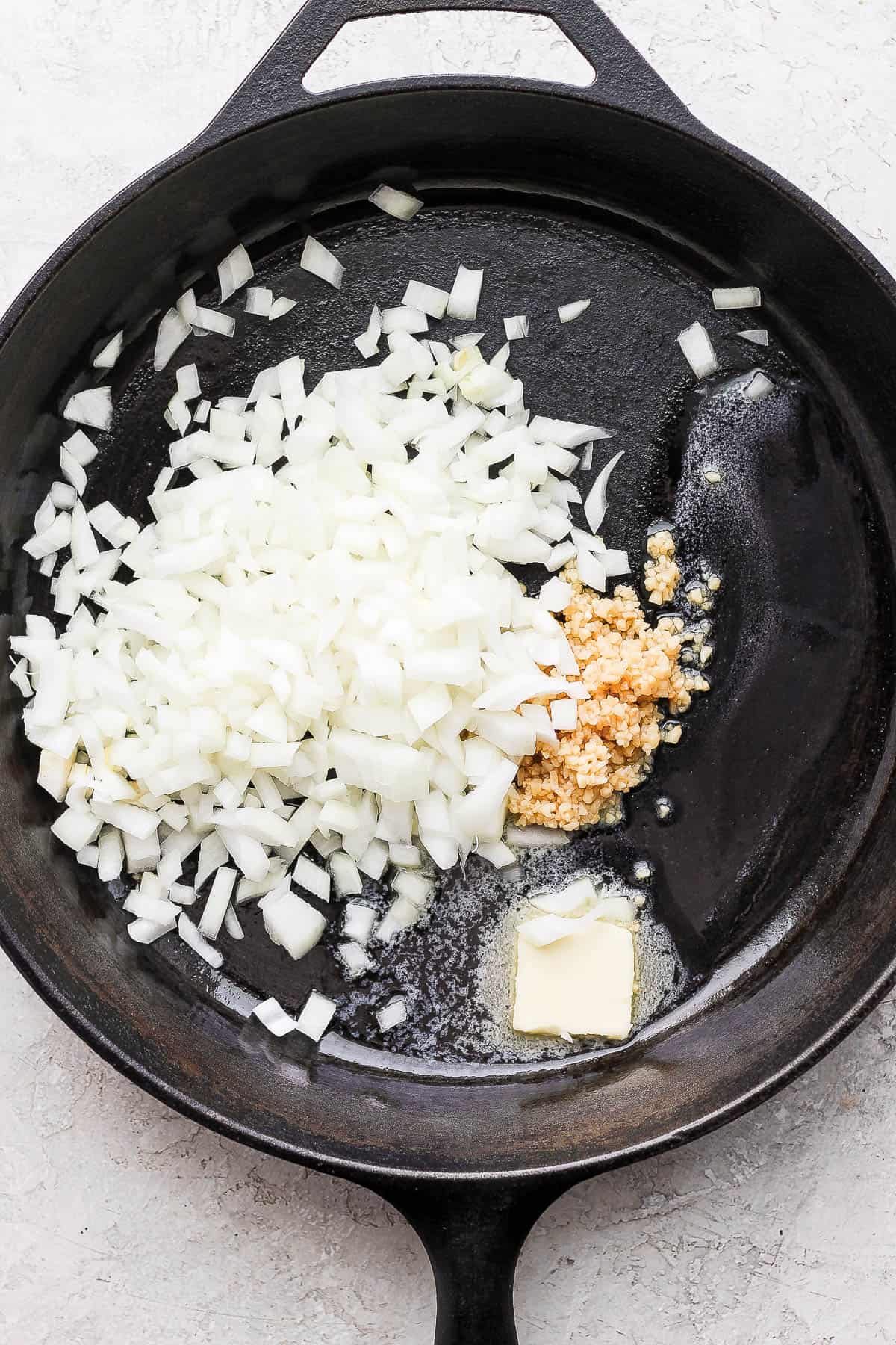 A cast iron skillet with melted butter, onion, and garlic.