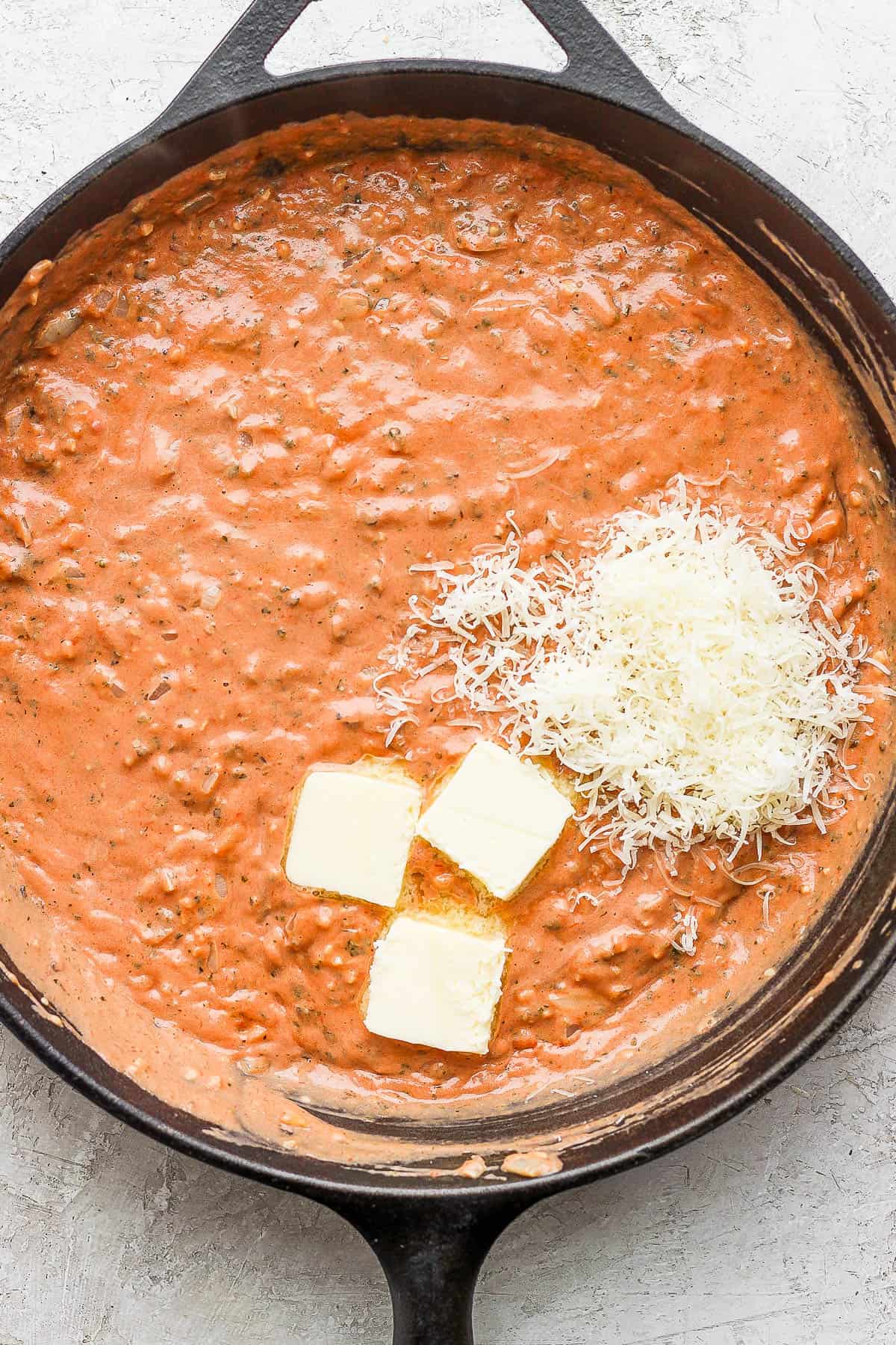 Tomato paste, pesto, and creamer mixed into the skillet with some butter and parmesan cheese on top.