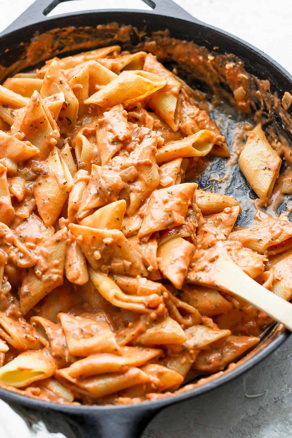 Creamy tomato pasta in the skillet with a wooden spoon.