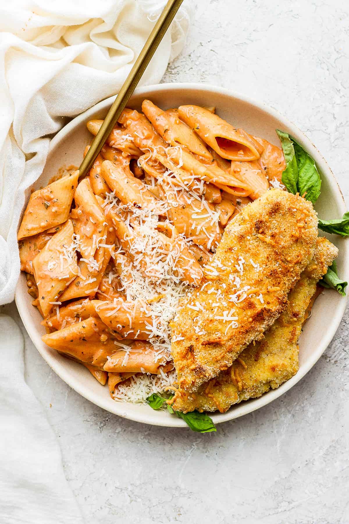 Creamy tomato pasta in a shallow dish with baked chicken cutlets.