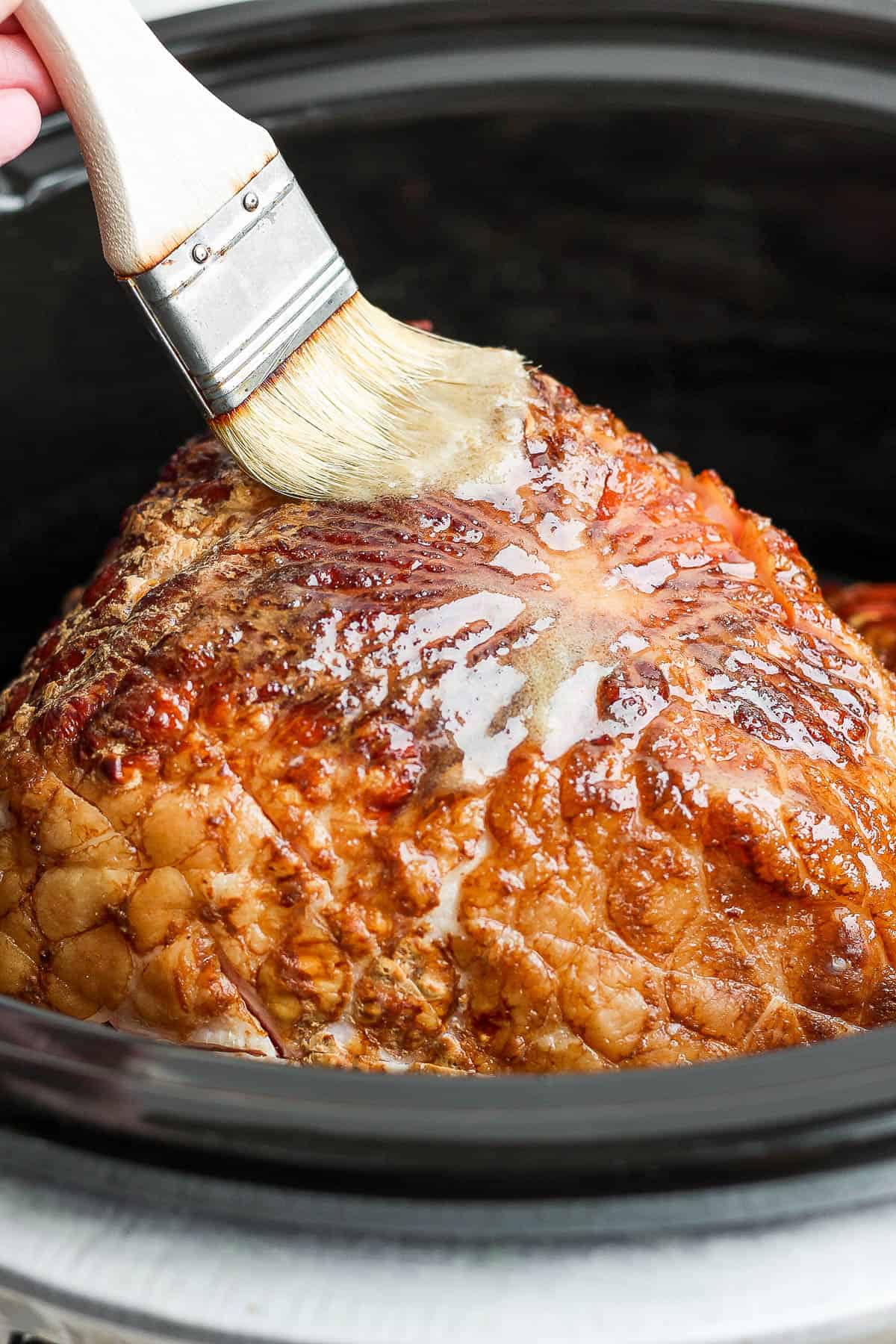 Ham being basted with the glaze in a crock pot.