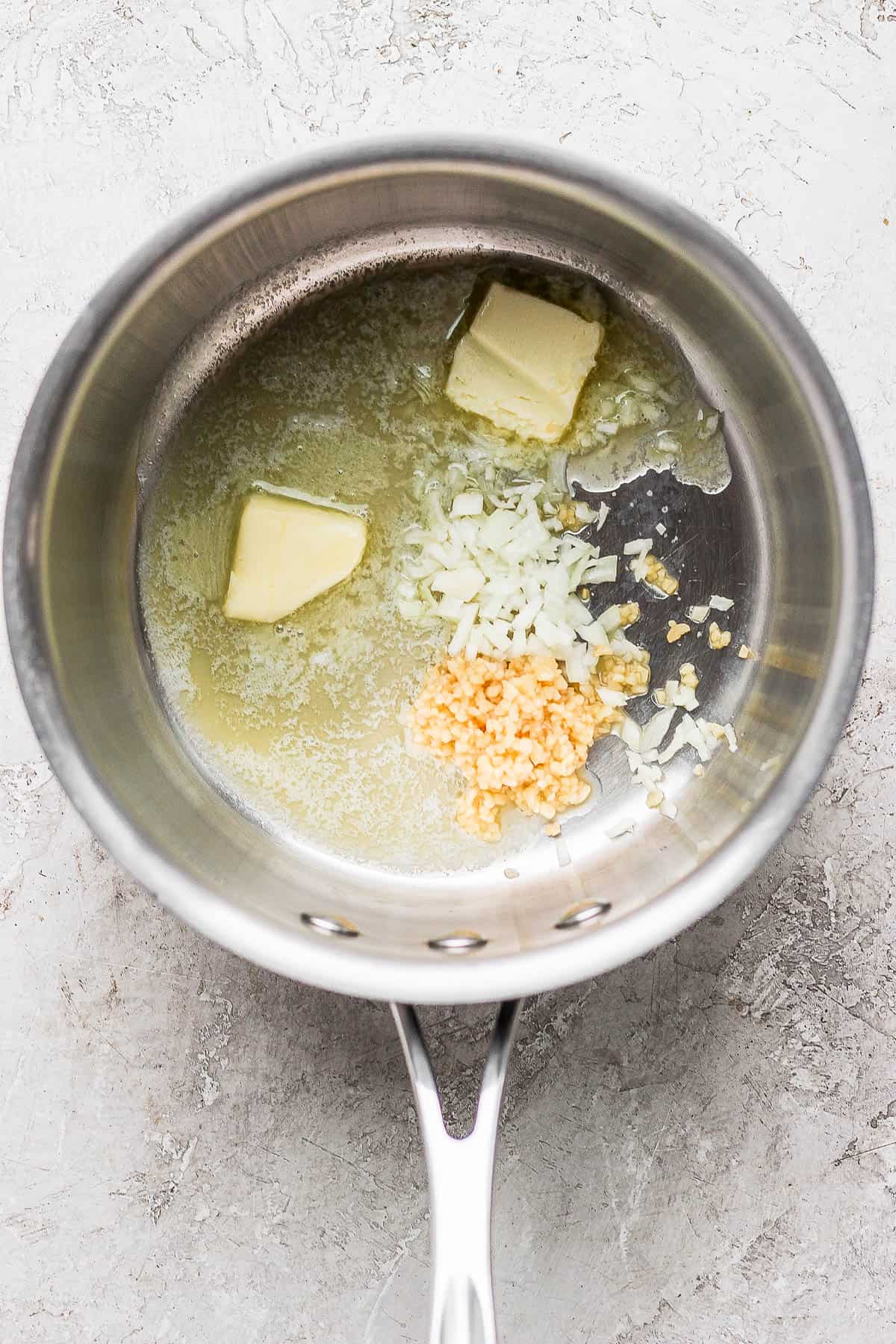 A saucepan with butter melting and garlic and onion added.