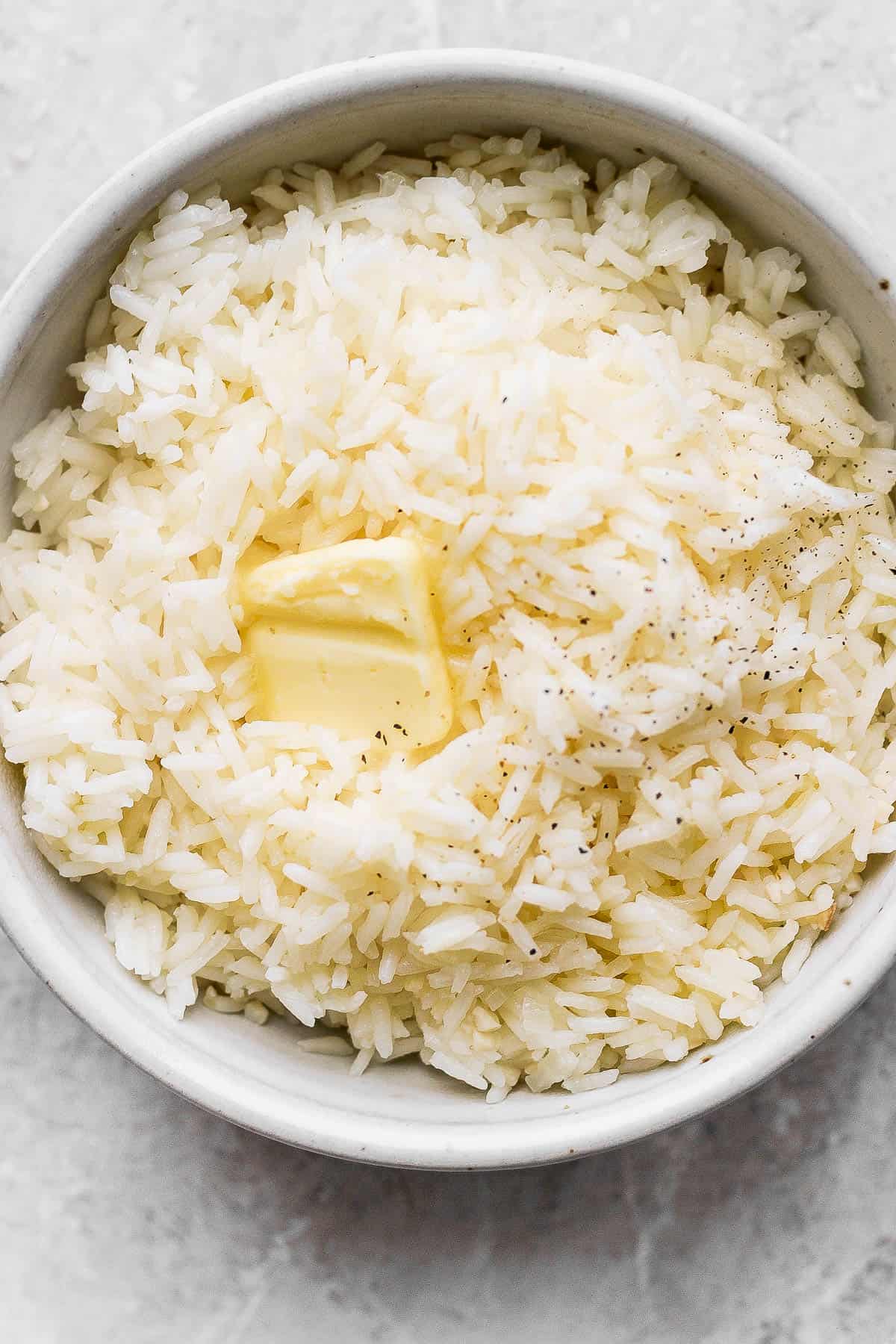 A bowl of buttery garlic rice with a pat of butter on top with a sprinkle of ground black pepper.