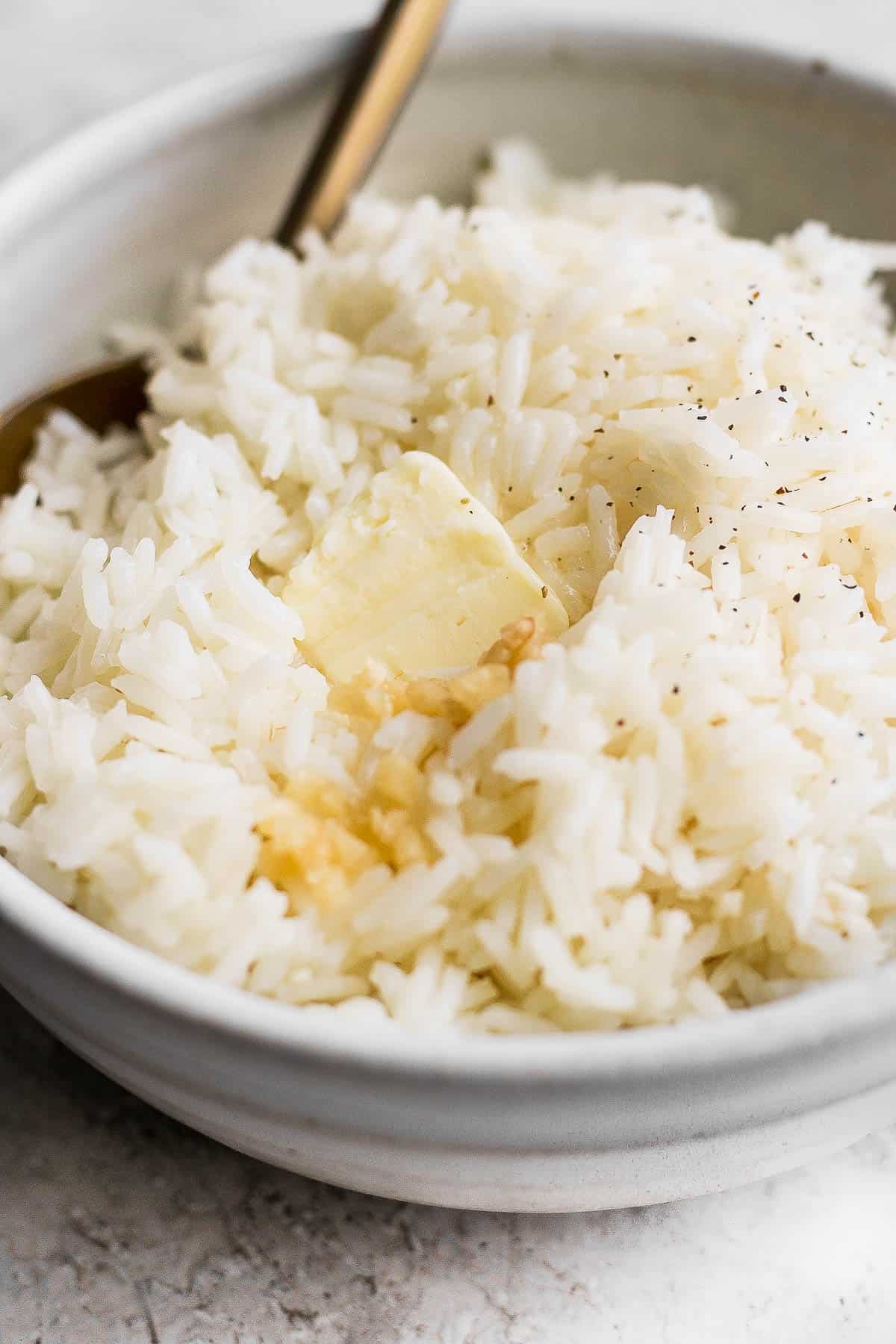 Garlic butter rice in a white bowl with a fork and a little extra butter on top.