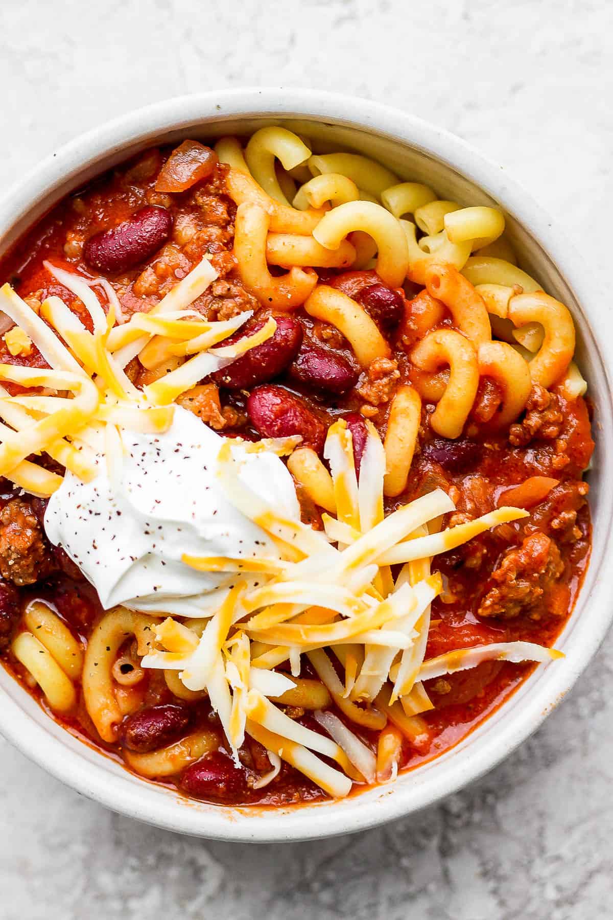 sour cream, shredded cheese, and pepper topped on a bowl of goulash and noodles.