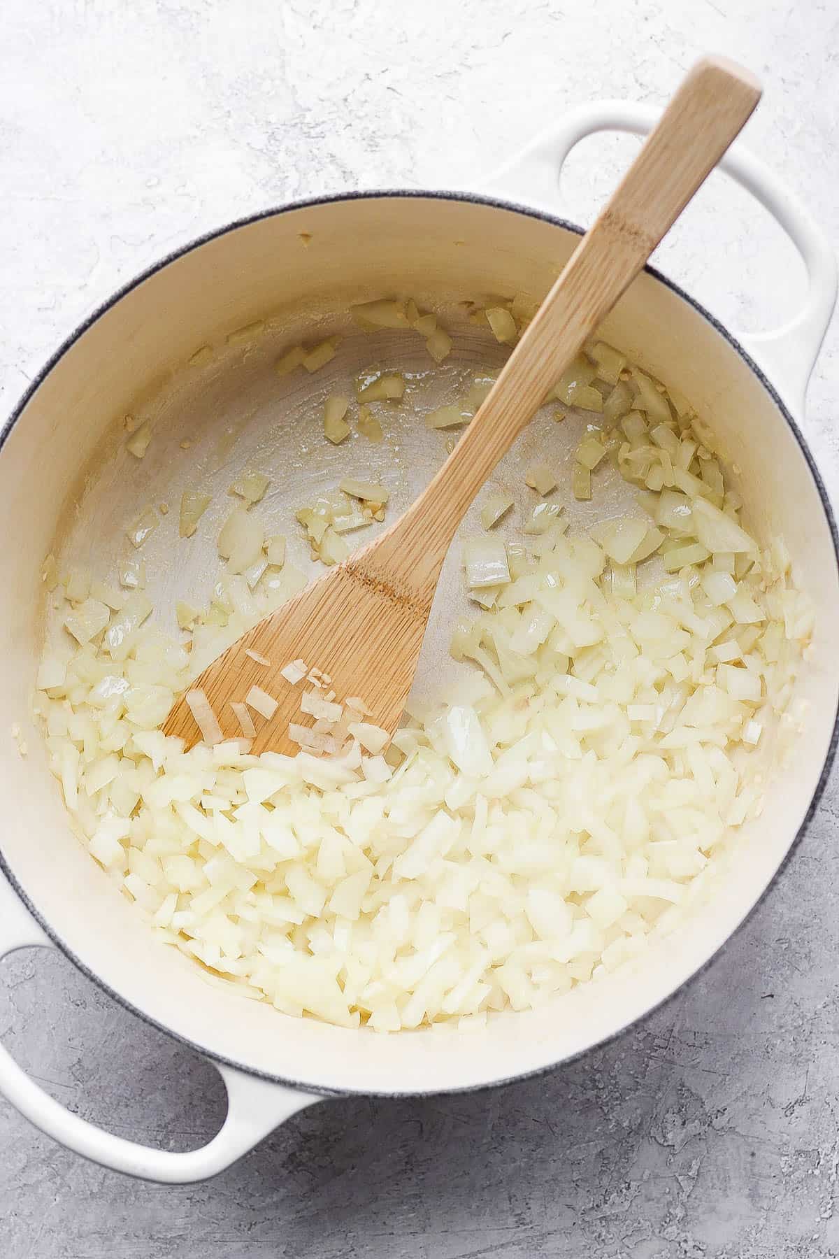 Diced onion and minced garlic in a dutch oven with a wooden spoon.