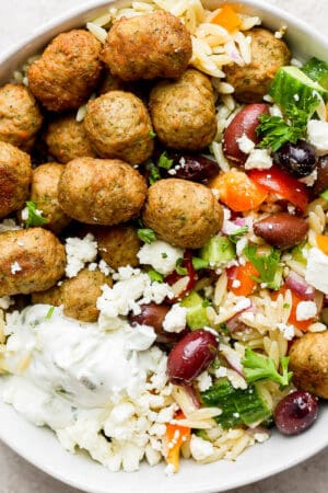 A bowl of greek orzo with greek turkey meatballs and some tzatziki sauce.
