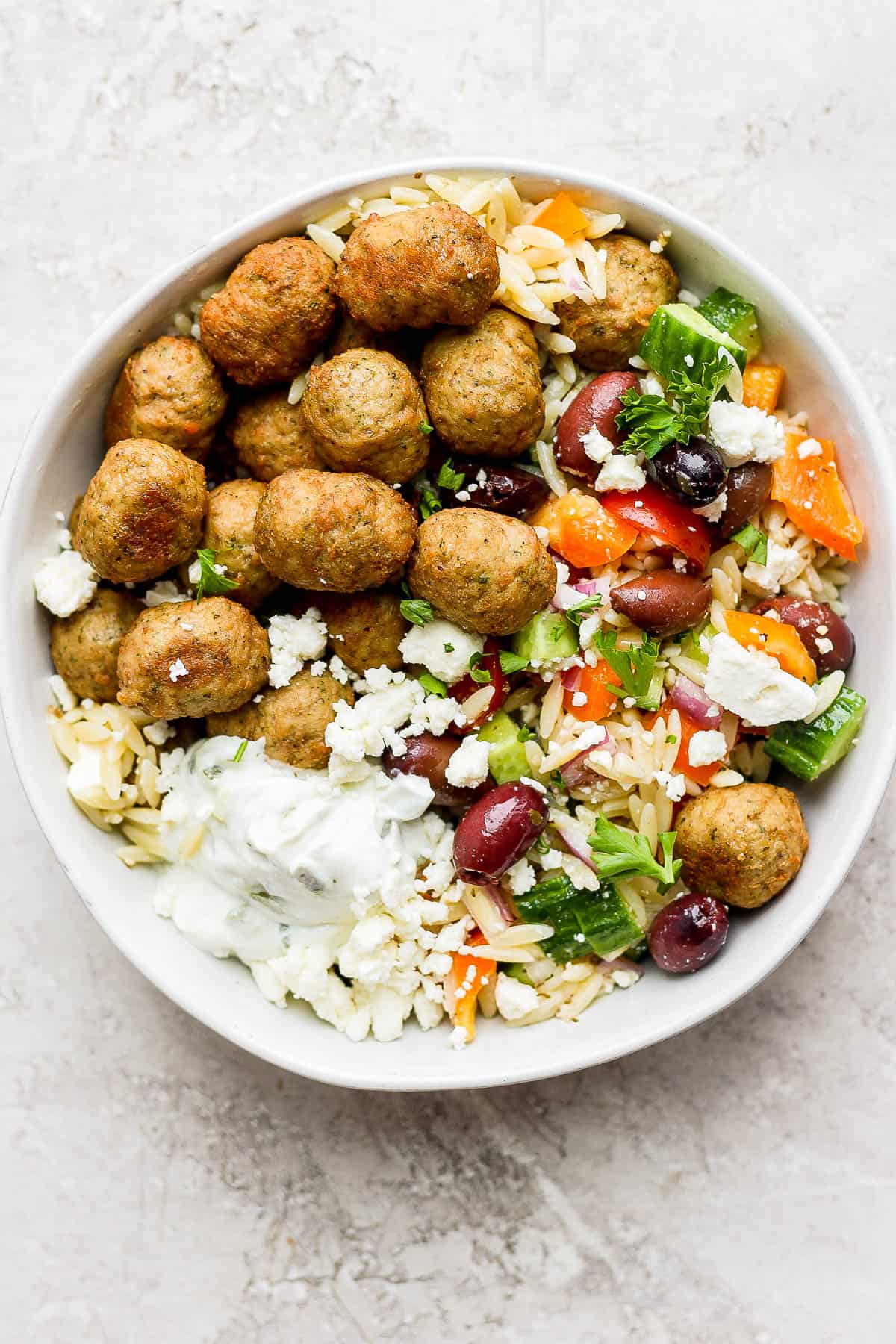 A bowl of greek turkey meatballs with greek orzo pasta and some tzatziki on top.
