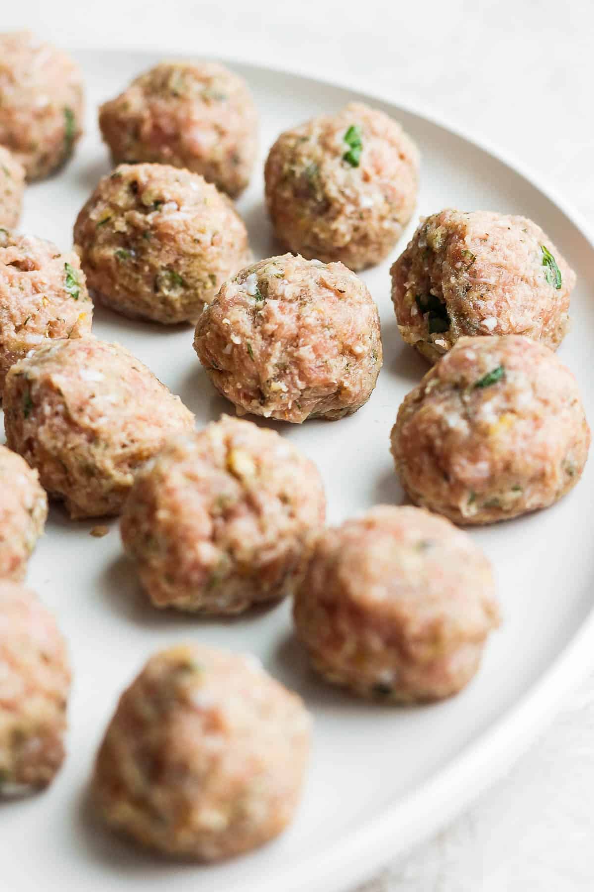 Raw meatballs on a white plate.