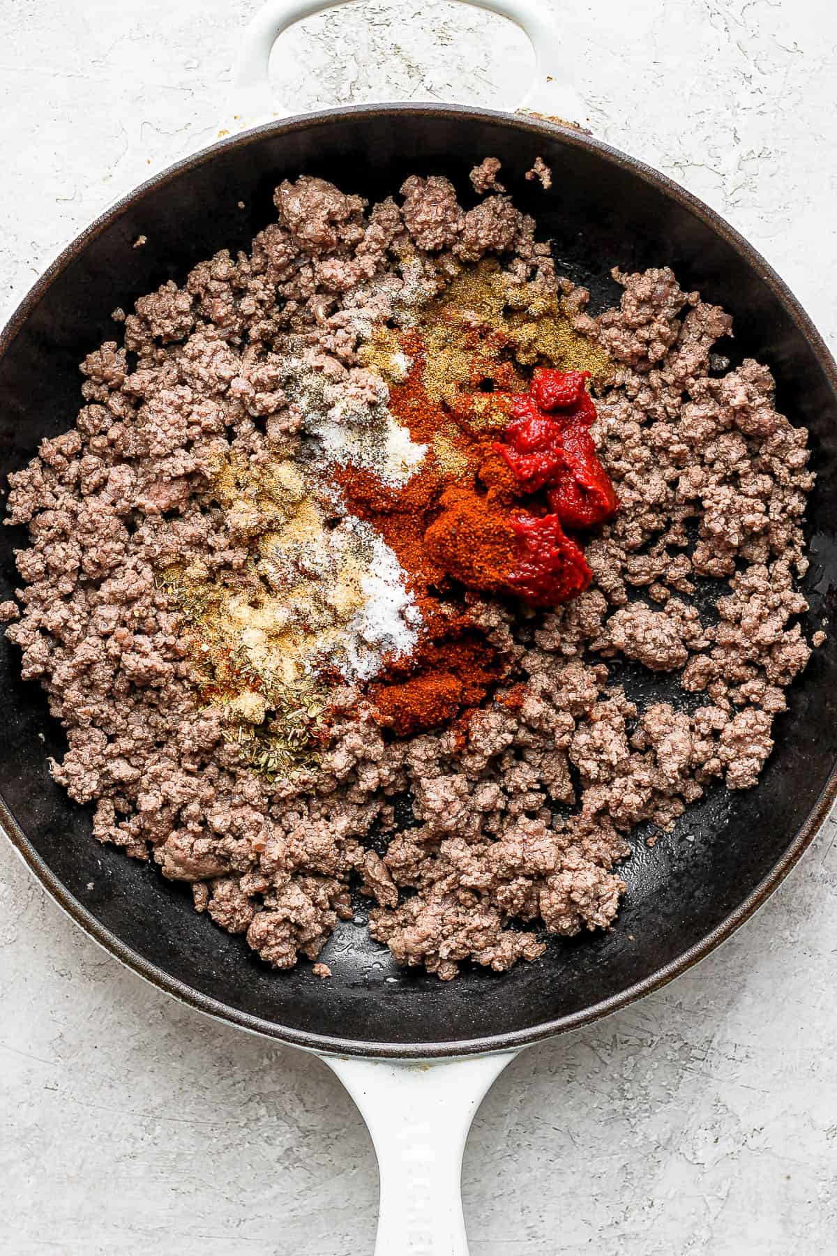 Ground black pepper, salt, cumin, chili powder, garlic powder, and onion powder on top of cooked ground beef in the skillet. 