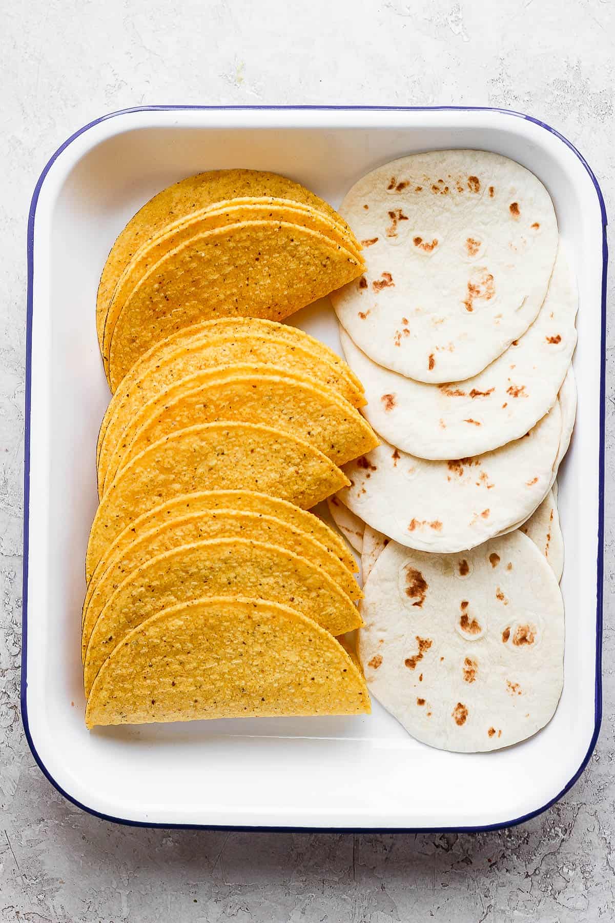 A casserole dish with flour tortillas and hard shell taco shells.