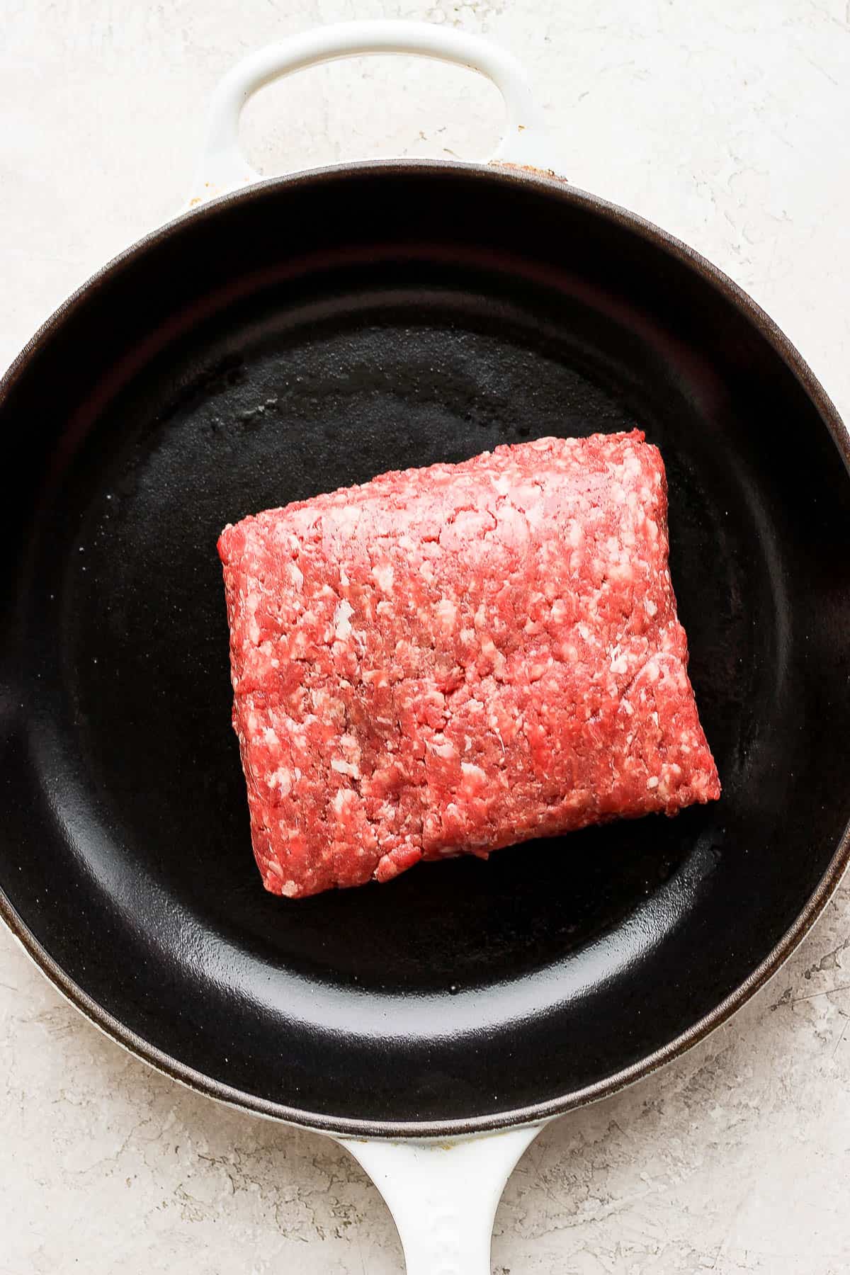 A chunk of raw ground beef in a cast iron skillet. 