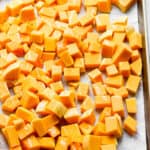 Cubed butternut squash on a baking sheet drizzled with olive oi.