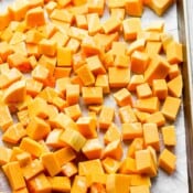 Cubed butternut squash on a baking sheet drizzled with olive oi.