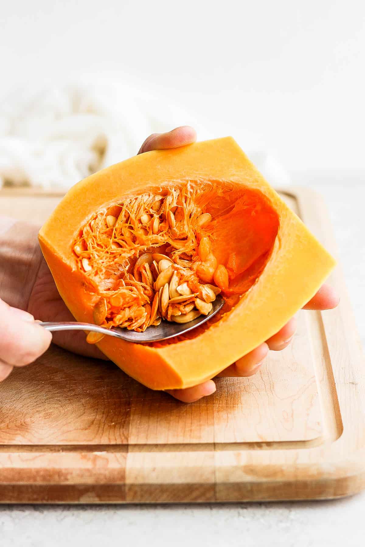 A spoon scooping the seeds and strings out of a butternut squash.
