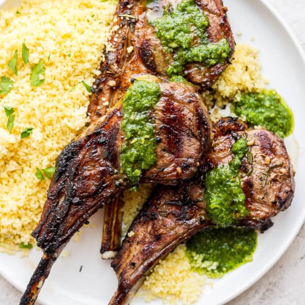 A plate of three grilled lamb chops on a plate with some mint chimichurri on top and some lemon couscous underneath it.