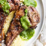 A close up of a grilled lamb chop on a plate with some mint chimichurri on top and some lemon couscous underneath it.