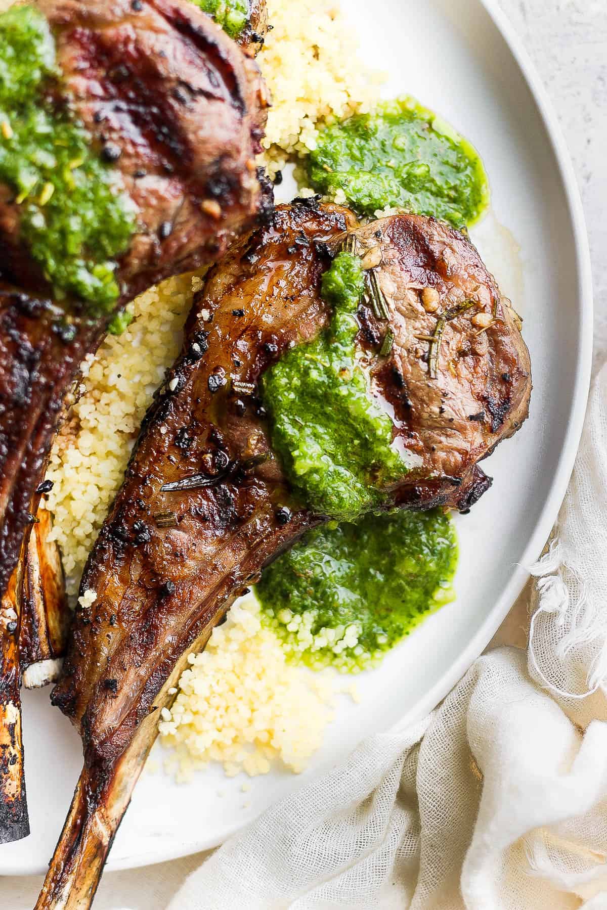 A plate of couscous topped with two grilled pork chops drizzled with mint chimichuri.