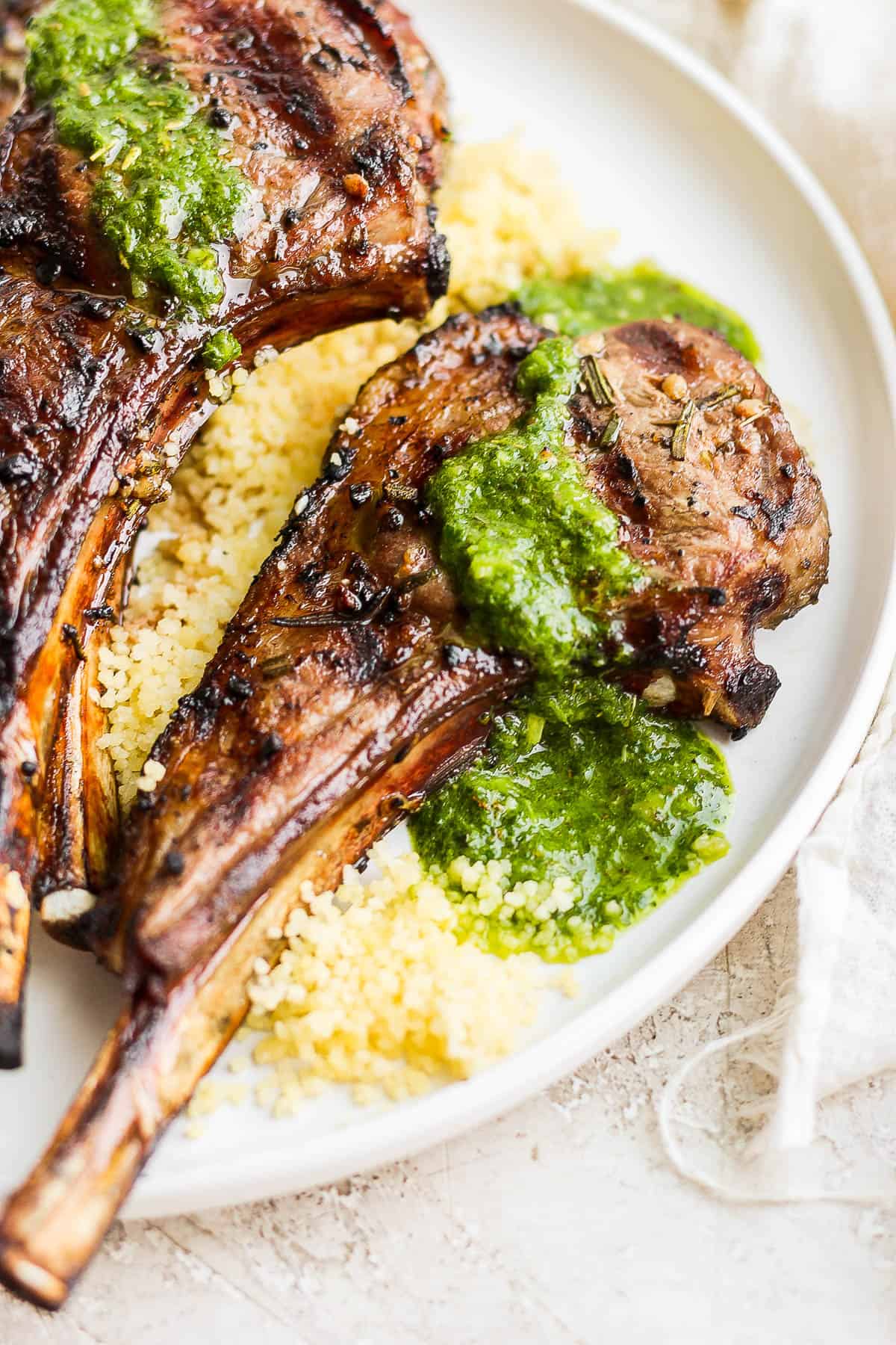 A close up of a grilled lamb chop on a bed of lemon coucous drizzled with mint chimichurri.