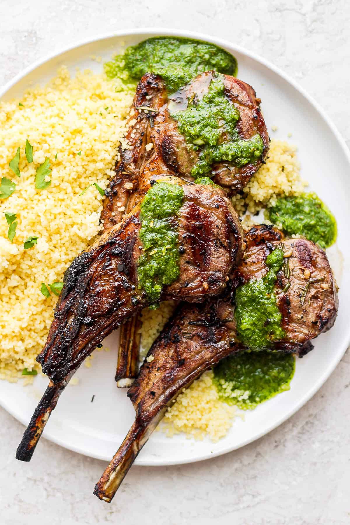 A plate with lemon couscous topped with three lamb chops drizzled with mint chimichuri.