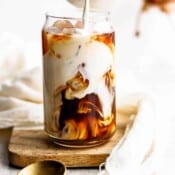 Someone pouring creamer into a class of iced coffee.