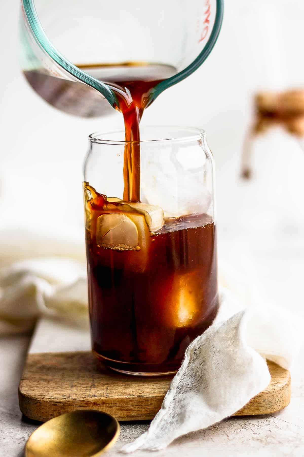 A measuring cup pouring coffee over ice in a glass jar.
