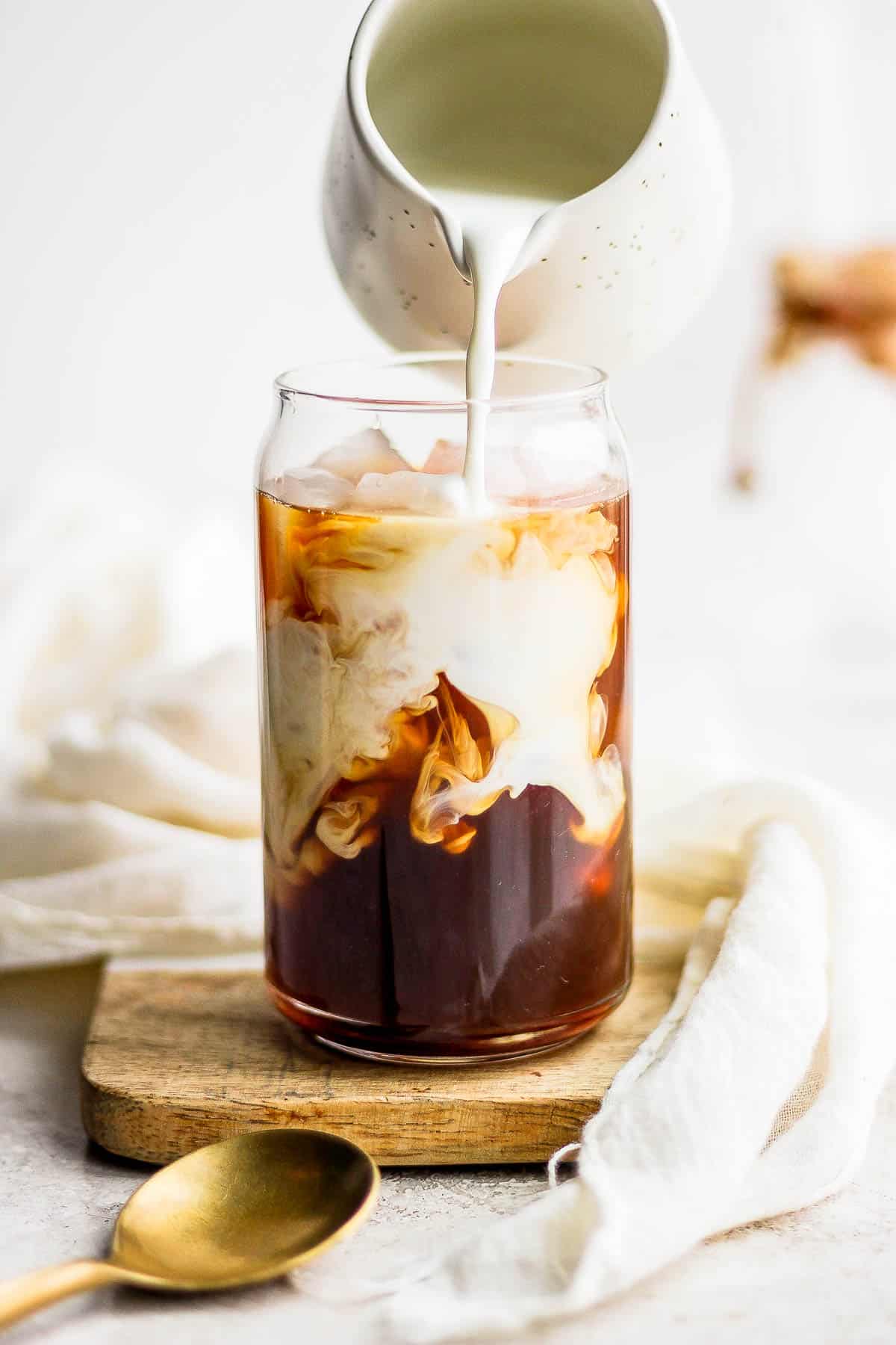 Creamer being poured into a glass of iced coffee.