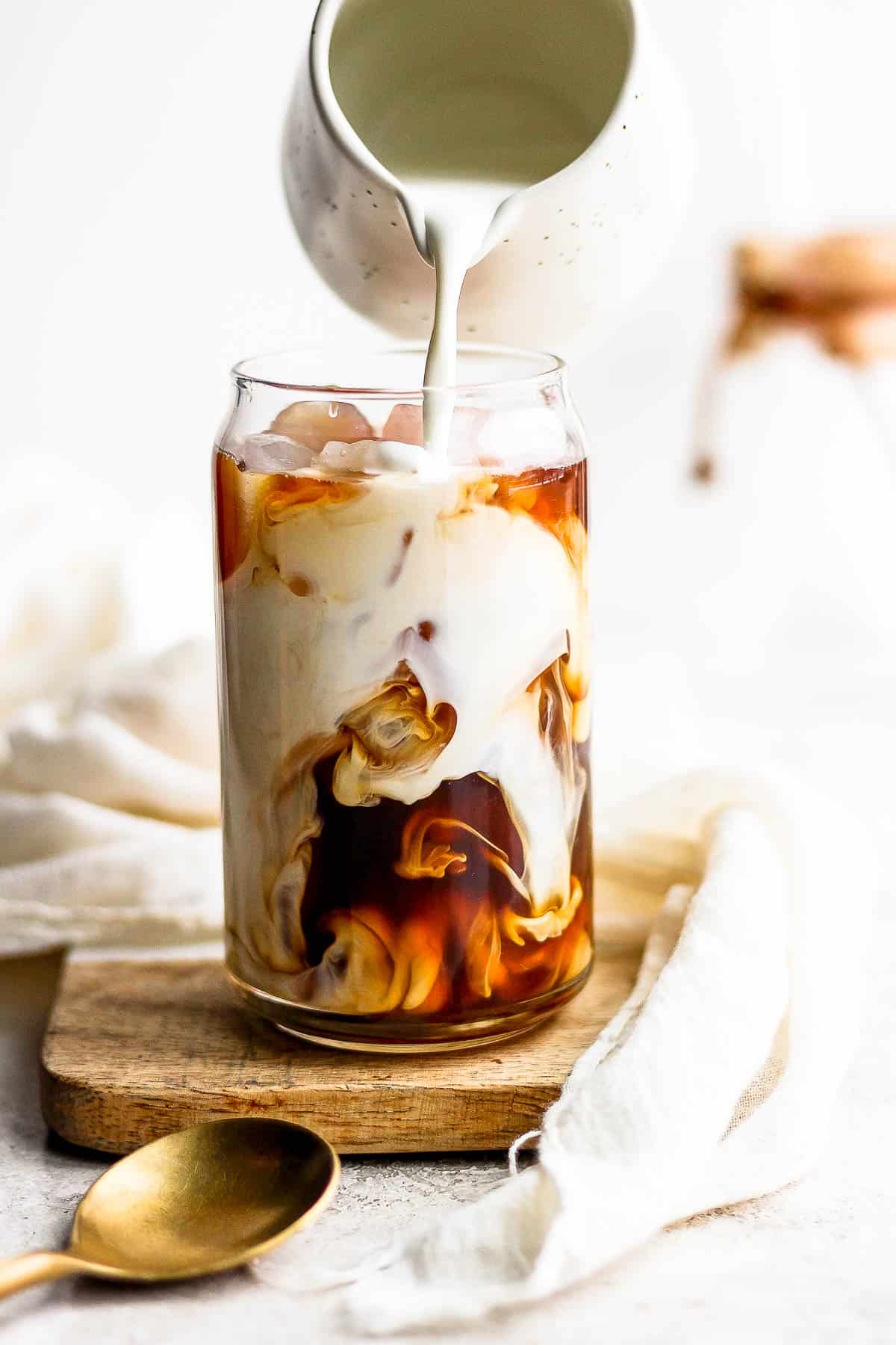 A container pouring cream over iced coffee in a glass.