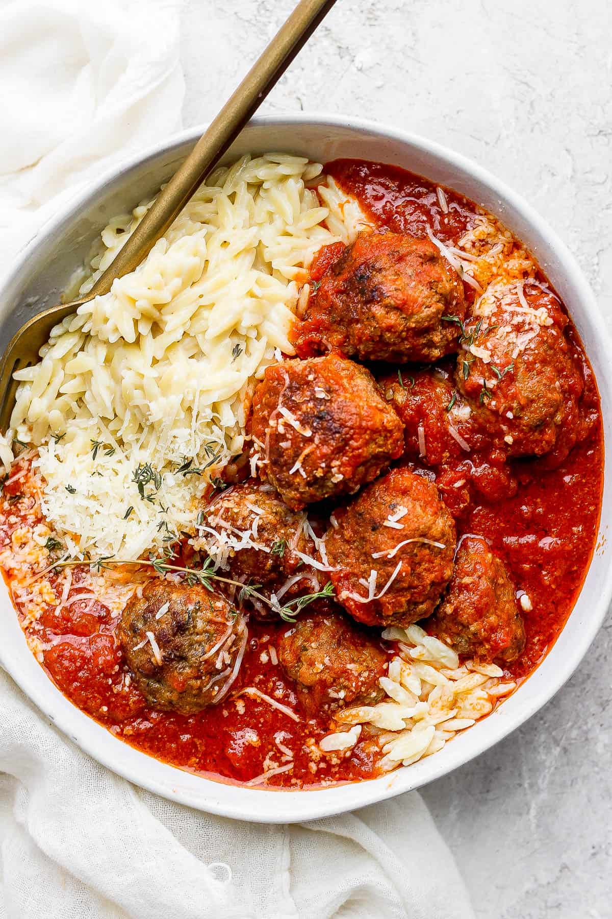 Italian meatballs in a white bowl with parmesan orzo and a spoon.