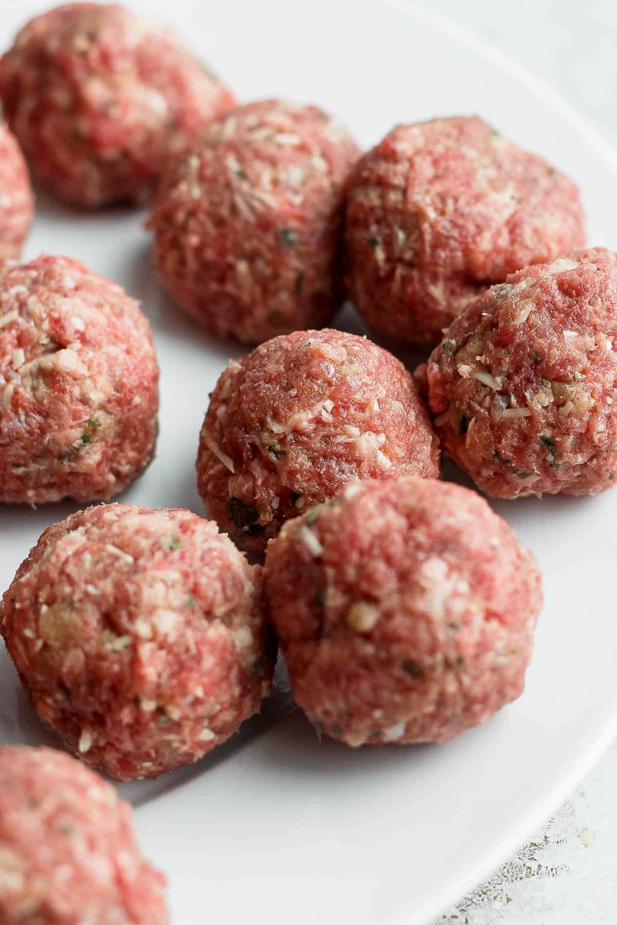 Rolled meatballs on a white plate before cooking.