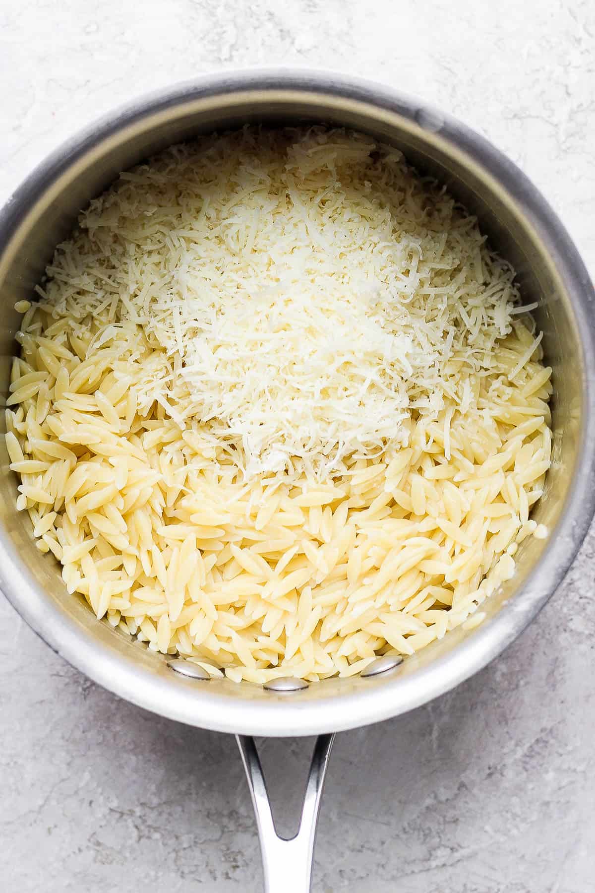 Cooked orzo in a saucepan with parmesan cheese added.