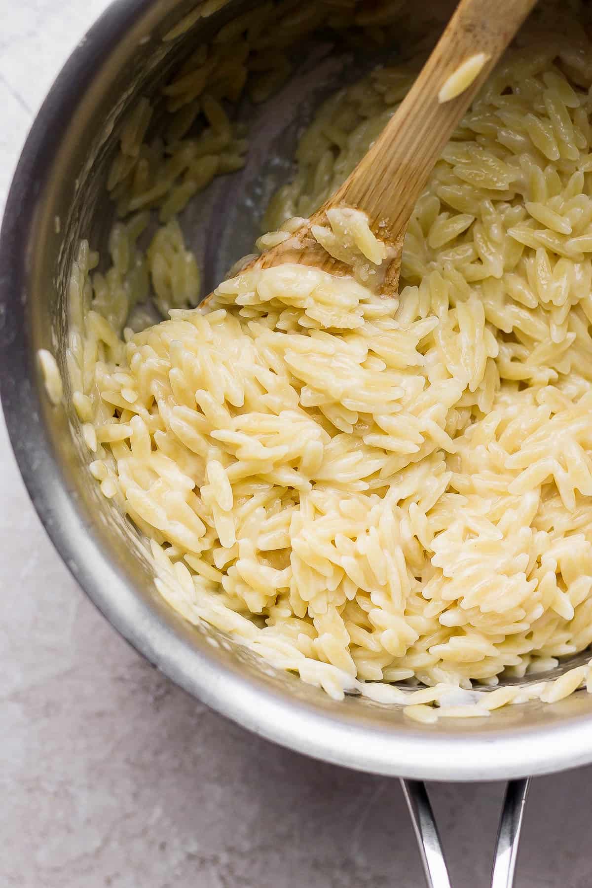 Parmesan orzo in a saucepan with a wooden spoon.