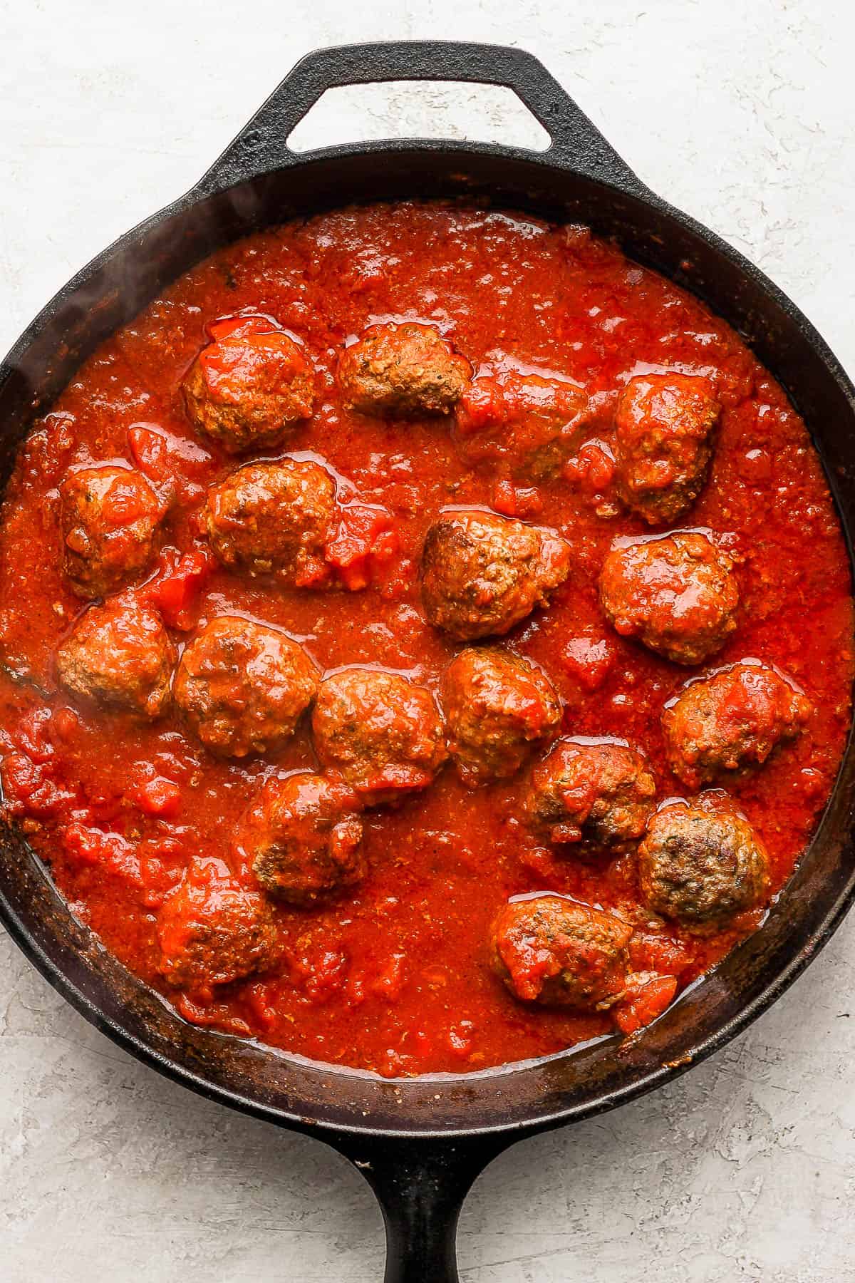 Meatballs with marinara sauce and diced tomatoes in a skillet.