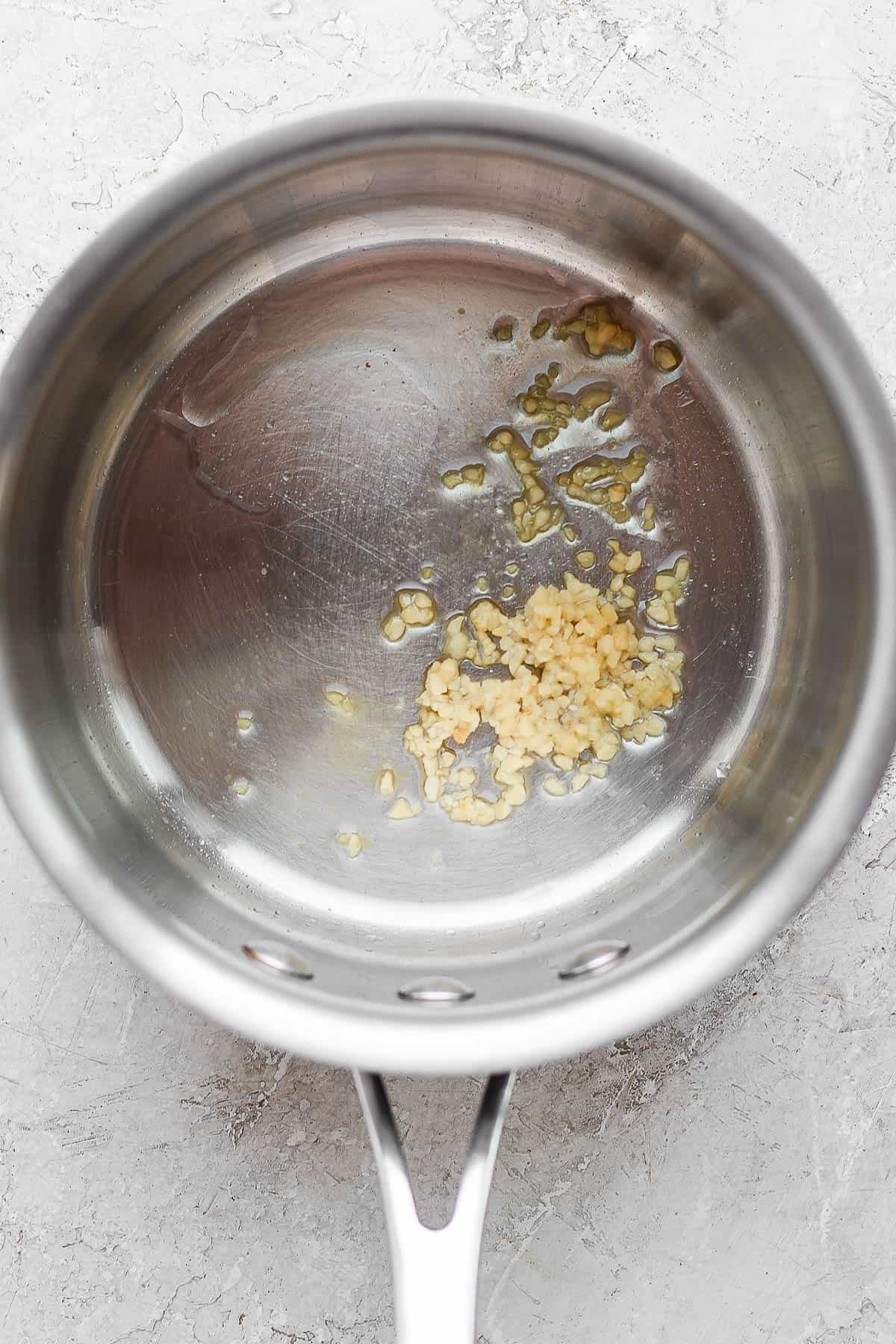A medium sauce pan with oil and minced garlic in the bottom.