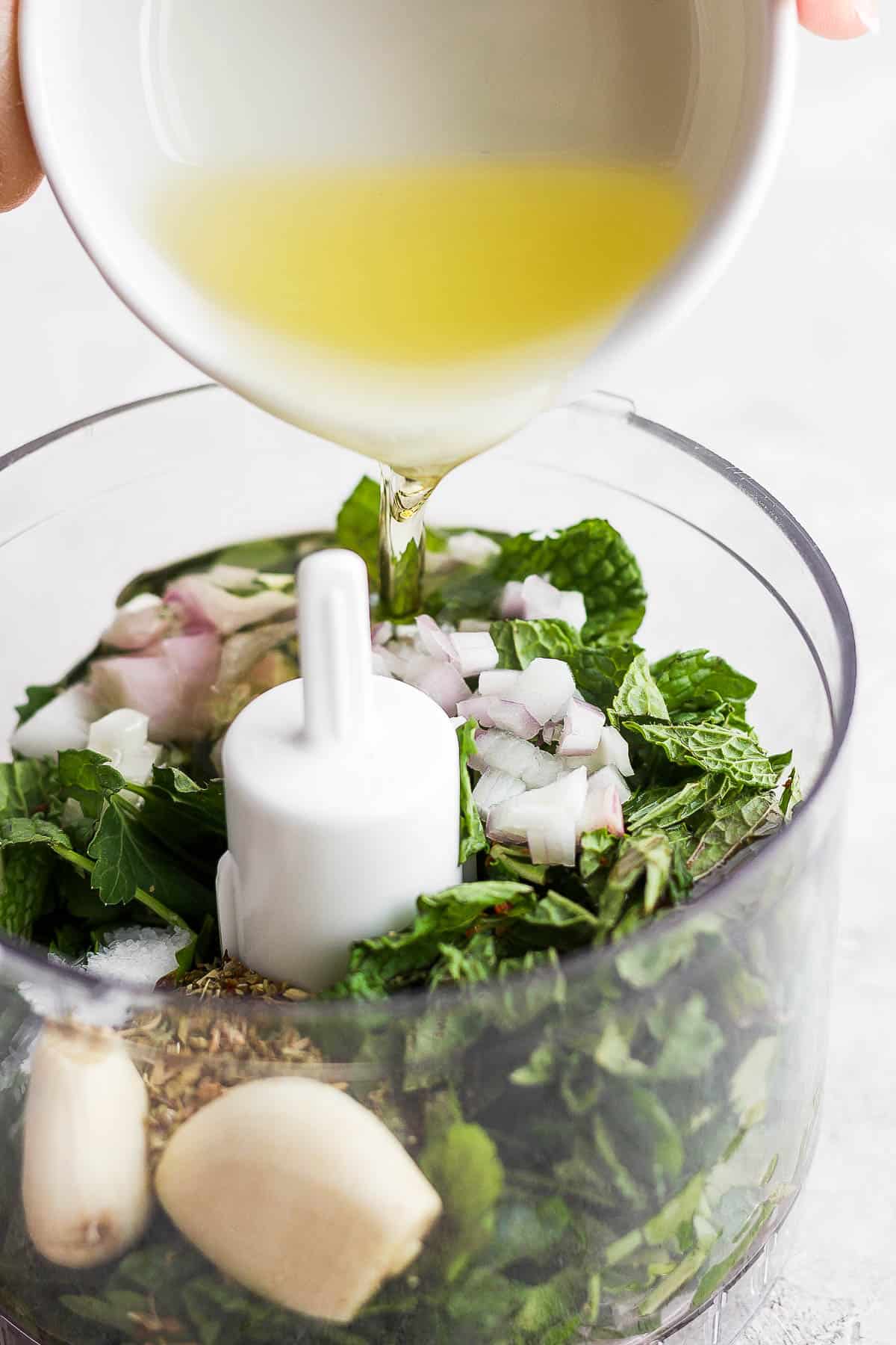 A hand pouring a small bowl of lemon juice into the food processor.