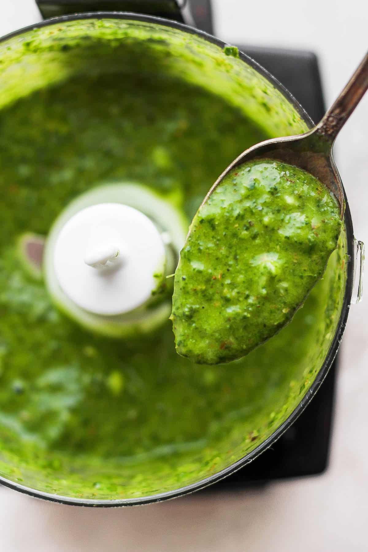 A spoon pulling out a scoop of mint chimichurri sauce from a food processor. 