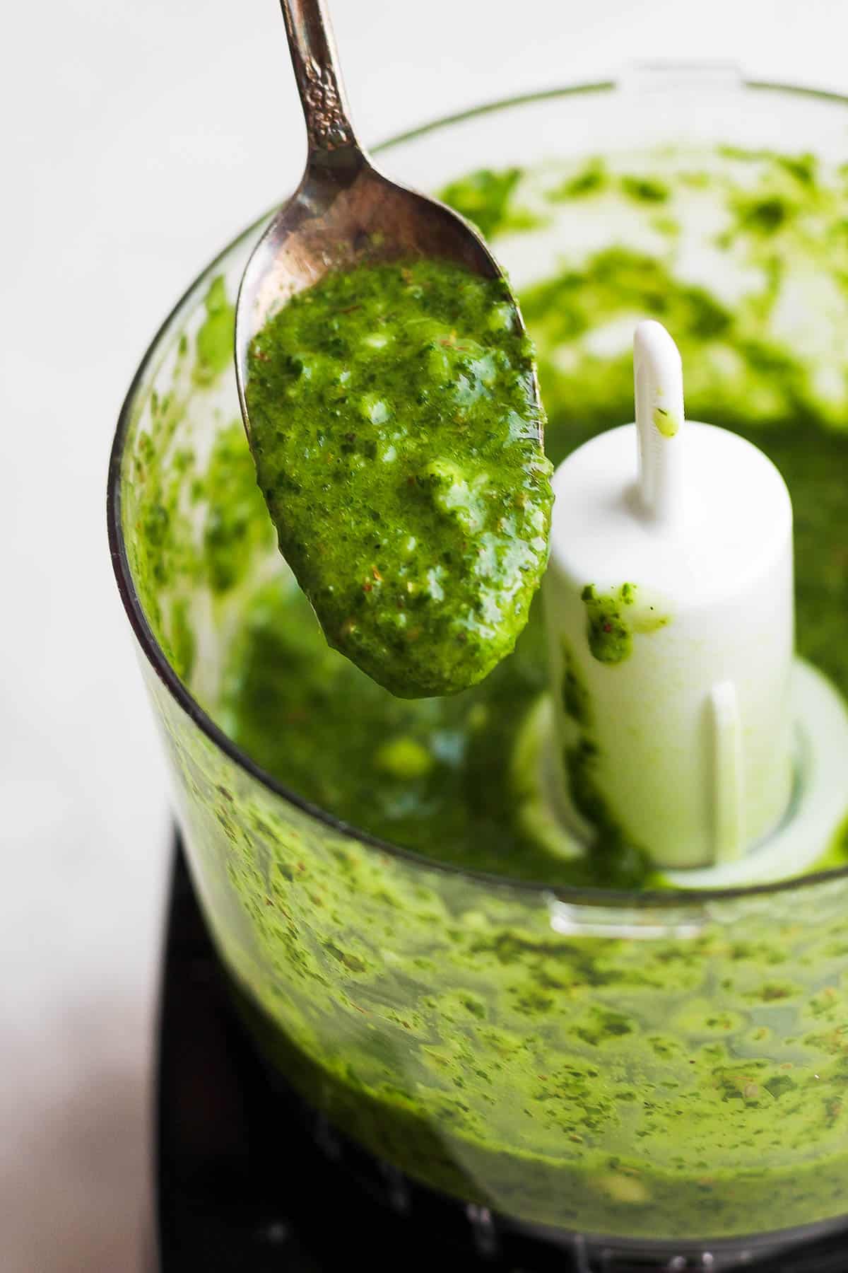 A spoon scooping out some of the sauce from the food processsor.