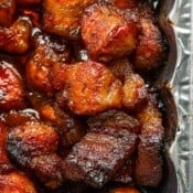 Close up top shot of a few pieces of pork belly burnt ends in a foil baking dish.