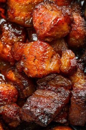 Close up top shot of a few pieces of pork belly burnt ends in a foil baking dish.