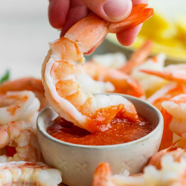 Someone dipping shrimp into some shrimp cocktail sauce.