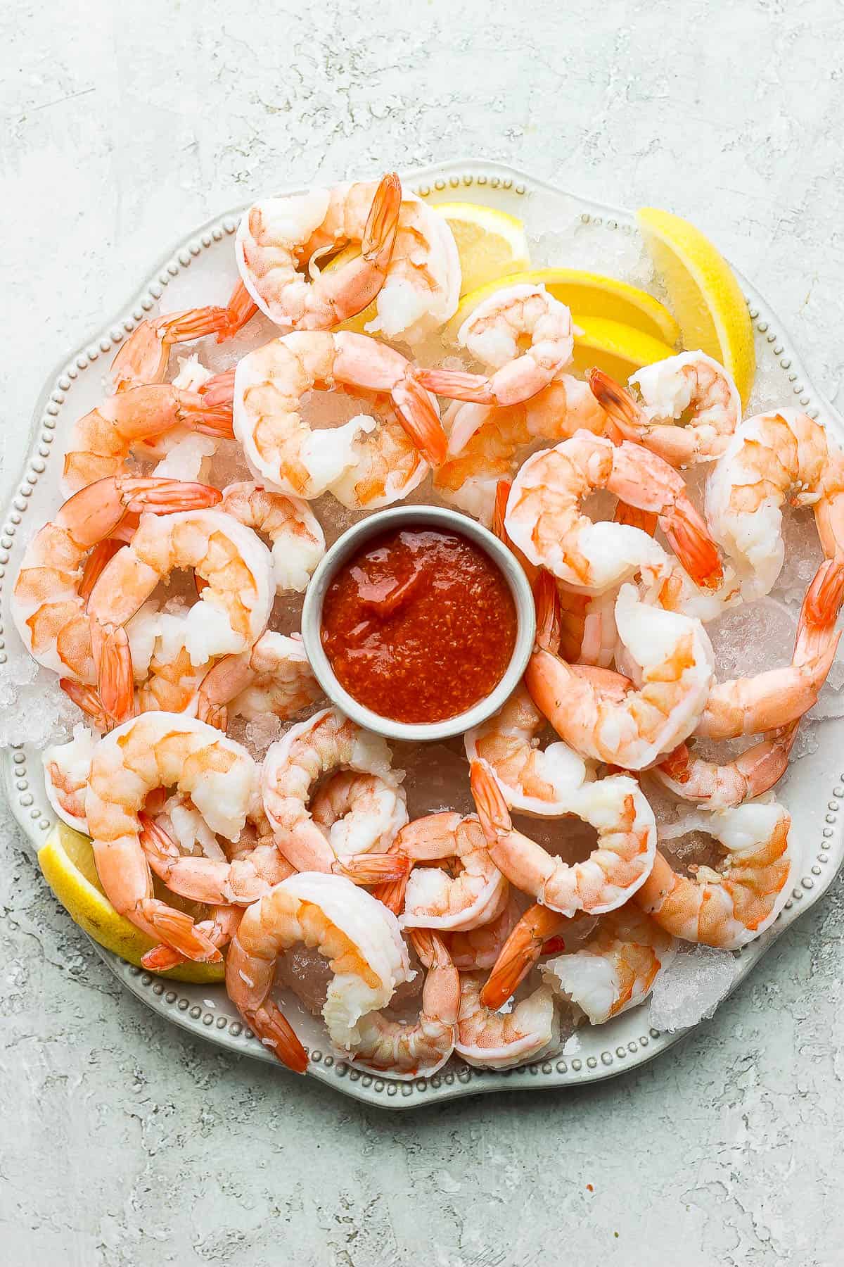 A platter of shrimp on a bed of ice, garnished with lemon wedges and a small bowl of shrimp cocktail in the middle.