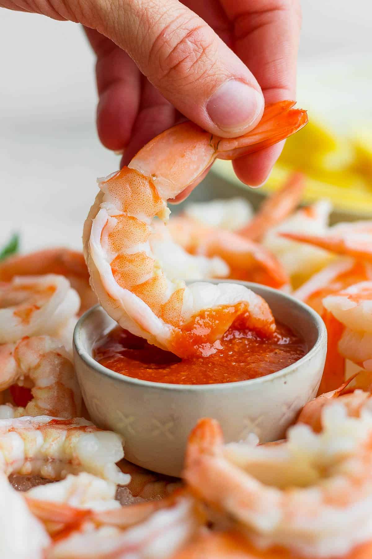 A hand dipping a shrimp into the cocktail sauce.