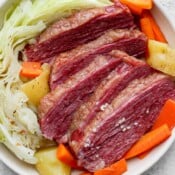 Smoked corned beef cut into large slices in a white bowl with cabbage, potatoes, and carrots.