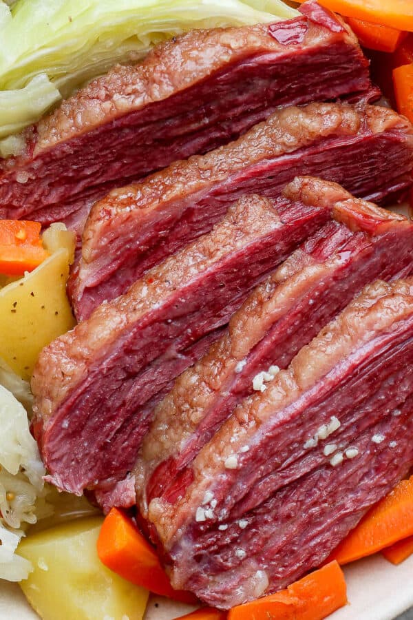 Smoked corned beef cut into large slices in a white bowl with cabbage, potatoes, and carrots.