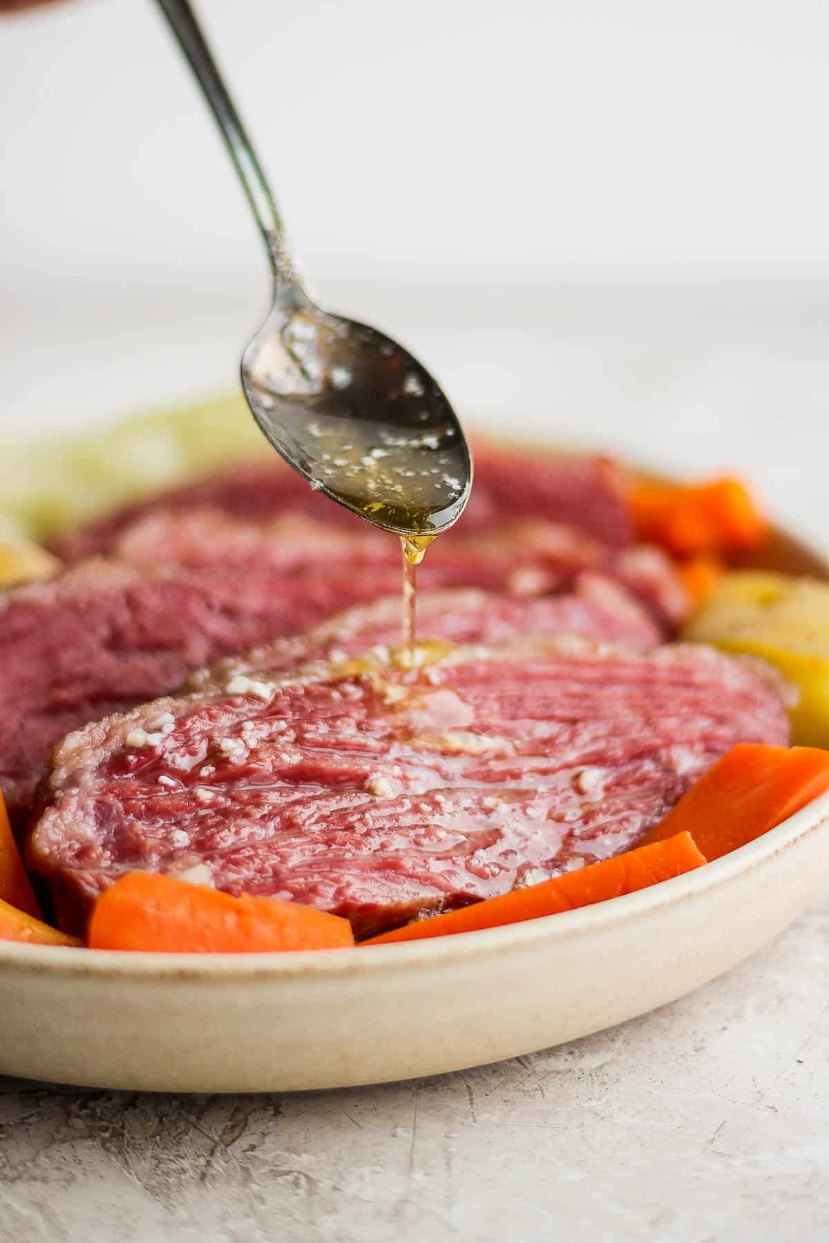 A spoon drizzling smoked butter on top of smoked corned beef brisket.