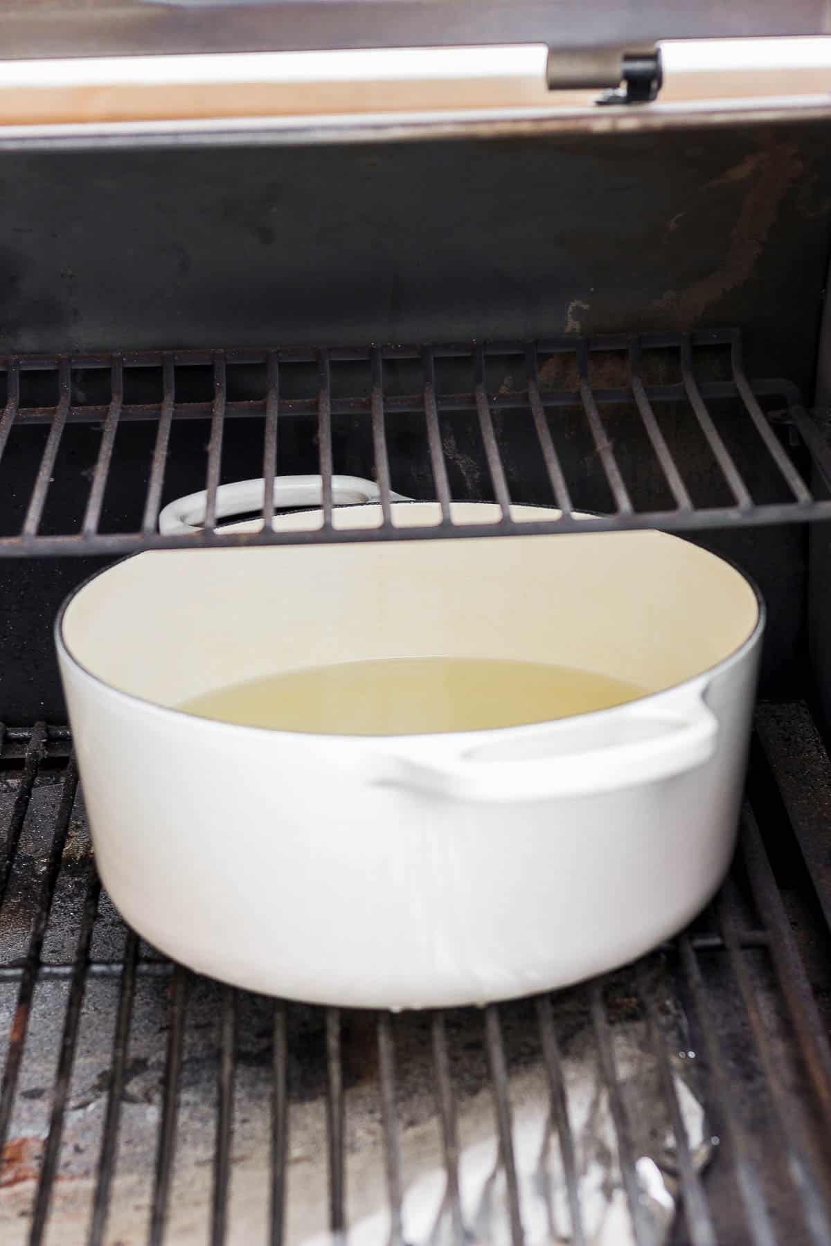 A large dutch oven with water and chicken broth on the smoker.