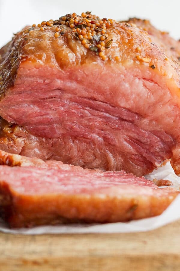 A smoked corned beef sitting on a piece of parchment on top of a wooden board with one slice sitting in from of the rest of the roast.